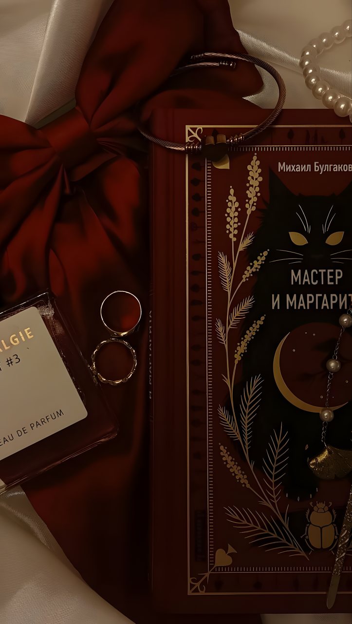 Dark burgundy still life with The Master and Margarita book by Mikhail Bulgakov, a perfume bottle, red fabric, jewelry, pearls, and botanical details.