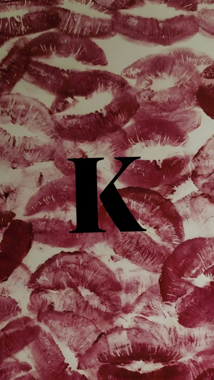 A large black letter K appears over a cream background covered with burgundy lipstick kiss prints.