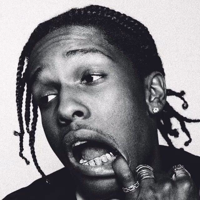 Black and white close-up portrait of Travis Scott with braided hair, jewelry, and an expressive open-mouth pose.