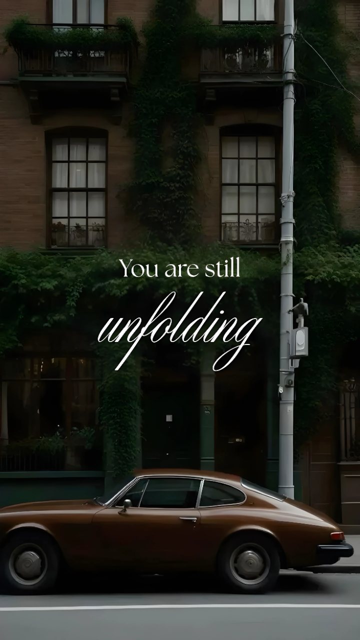 Brown vintage car parked beside an ivy-covered building with the quote “You are still unfolding” in elegant white lettering.